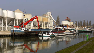 Figure 11 : Port de Bondy, sur le Canal de l’Ourcq. Le canal a fait l’objet de profonds remaniements depuis Girard. Il reste utilisé en navigation marchande (matériaux de construction et gravas notamment) sur sa partie à grand gabarit, 10 kms sans écluses jouxtant Paris, avec 4 ports. Ici, celui de Bondy (image WikiCommons, 2011, auteur Pline)